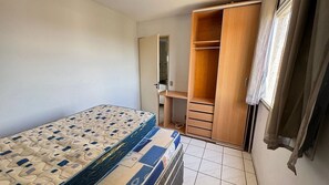 A bedroom with a bed, a wooden wardrobe, and a small desk.