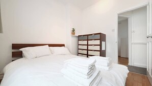 Un letto ben rifatto con lenzuola bianche, una testiera in legno e una piccola pianta su uno scaffale.