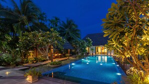 Una piscina con borde de baldosas, rodeada de plantas tropicales y palmeras.