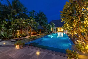 A swimming pool with a tiled deck, surrounded by tropical plants and palm trees.