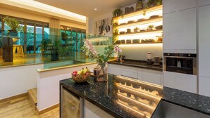 Una cocina moderna con zona de comedor de vidrio, plantas variadas y una isla central con frutero.