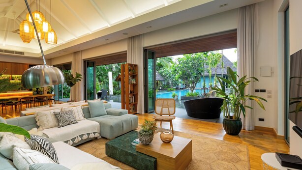 Una sala de estar moderna con un sofá modular, una mesita de centro y un ventanal con vista a una piscina y follaje.
