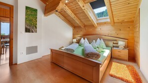 Un dormitorio con techo de madera, una cama, una mesita de noche, una lámpara de pared y una ventana.