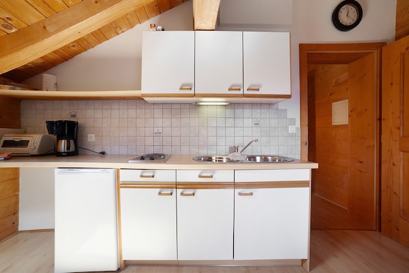 Una cocina con armarios blancos, lavavajillas, cafetera y un reloj en la pared.