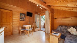 Interior de una cabaña de madera con comedor, sofá y televisor.