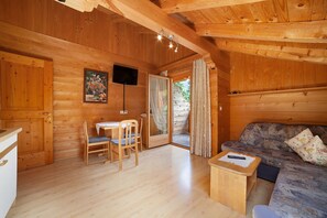 Interior de una cabaña de madera con comedor, sofá y televisor.