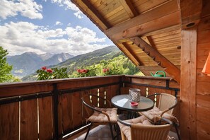 Un balcón de madera con una mesa y sillas, con vistas a un paisaje montañoso.