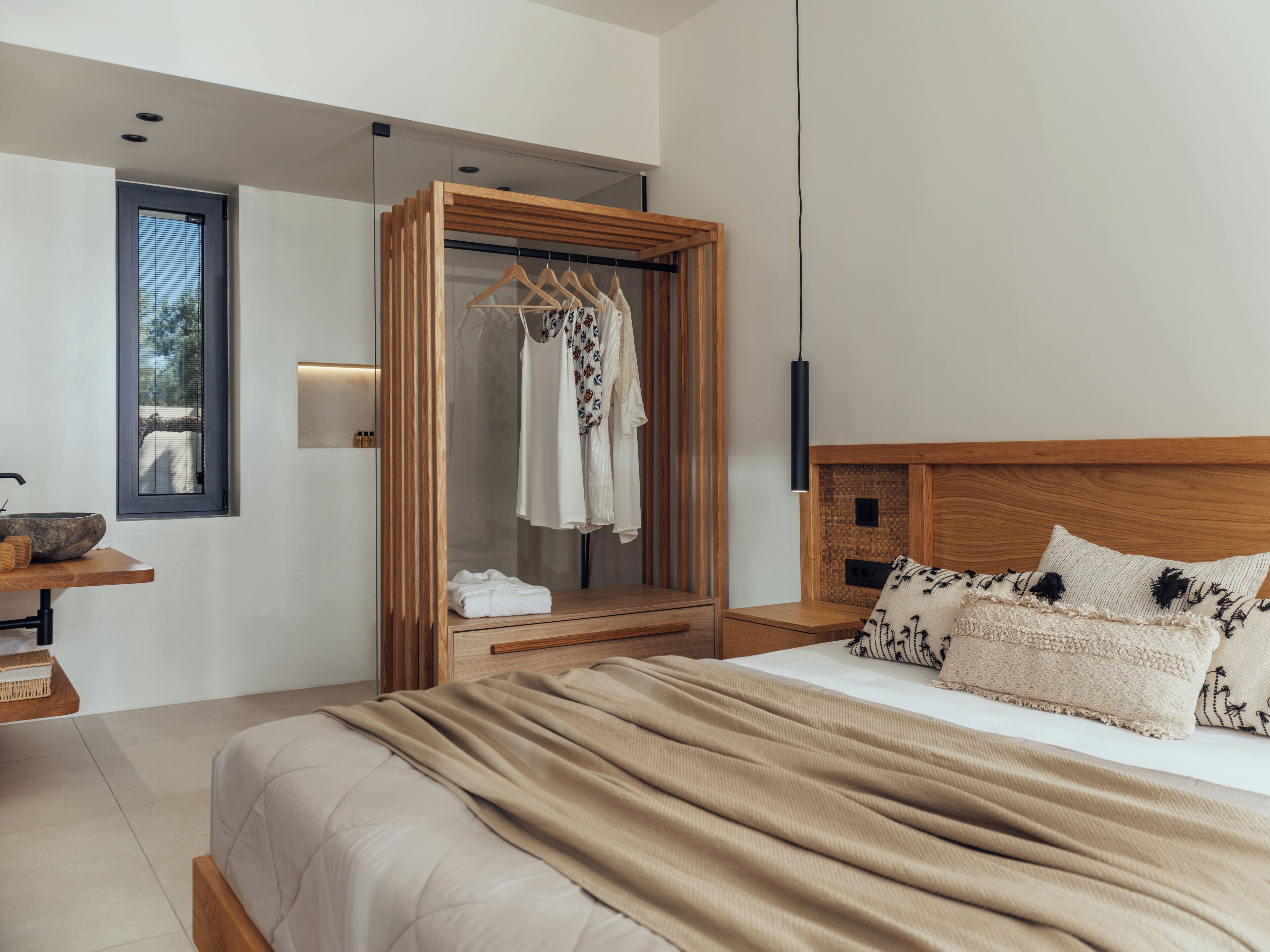 A modern bedroom with a large bed, a wooden wardrobe, a bedside table, and a window with blinds.