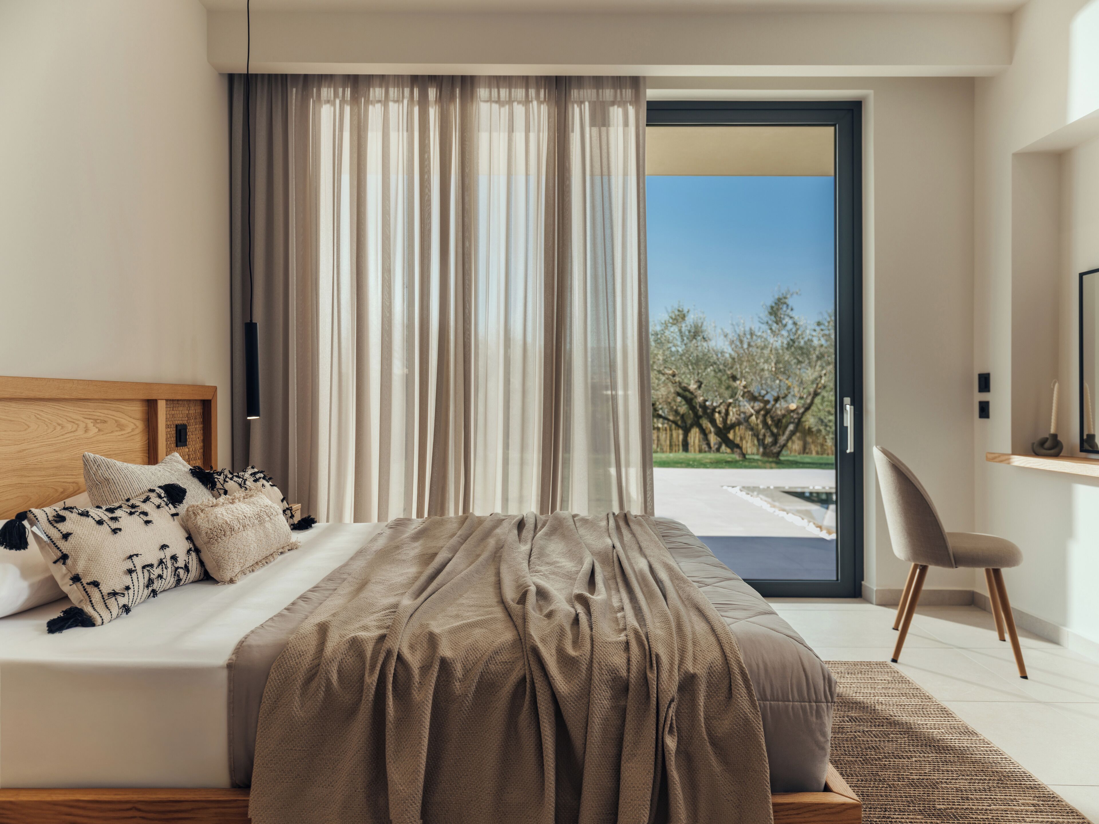 A modern bedroom with a large bed, a view through a sliding door, and a wooden headboard.