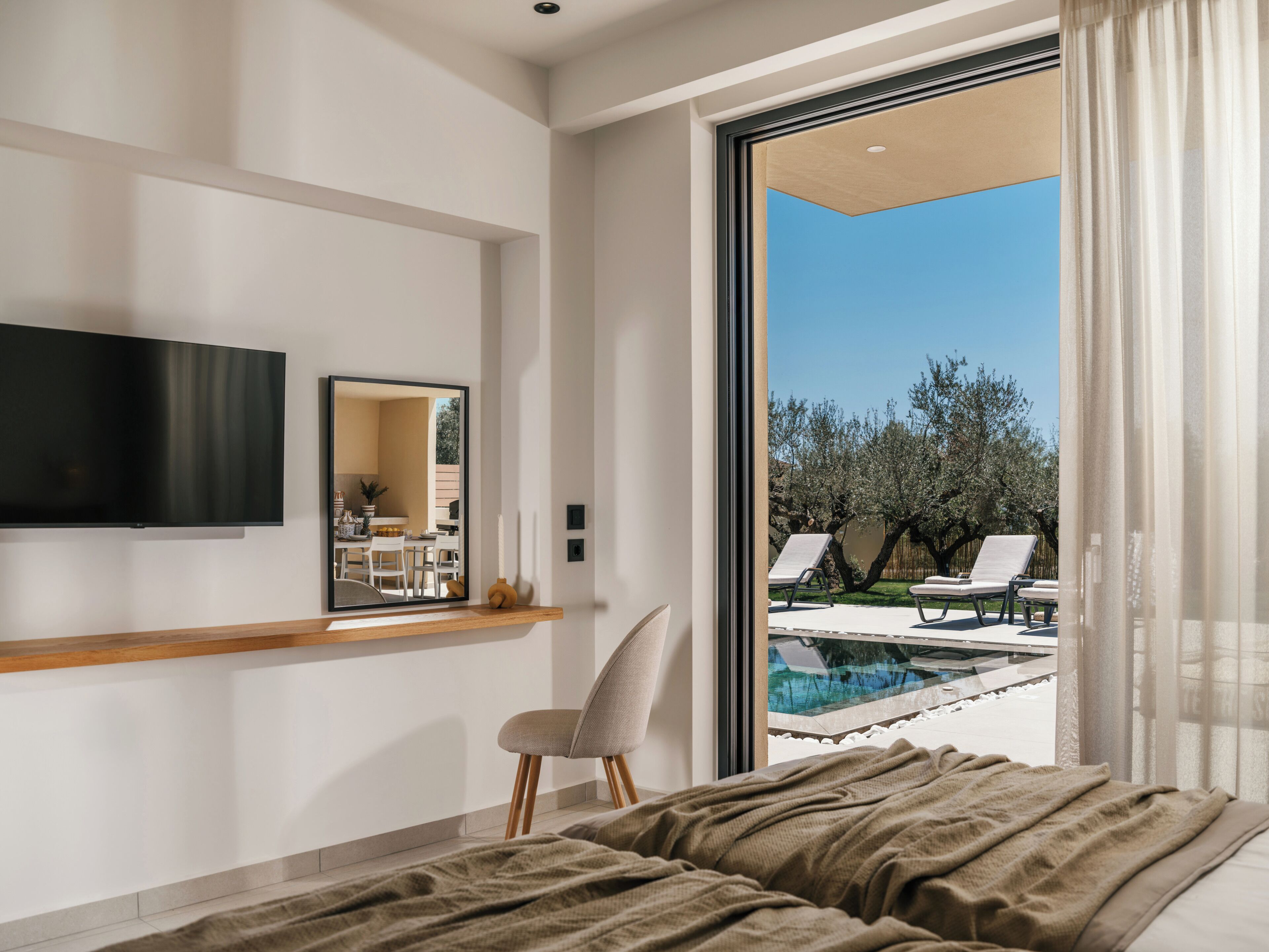 A bedroom with a bed, a TV, a mirror, and a view of an outdoor pool area.
