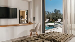 Un dormitori amb llit, televisió, mirall i vista a una zona de piscina exterior.