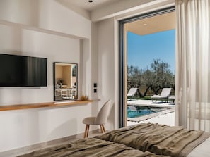 Ein Schlafzimmer mit Bett, Fernseher, Spiegel und Blick auf einen Außenpool.
