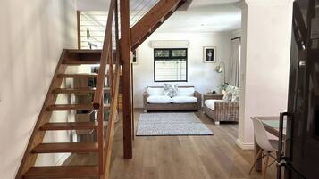 Un intérieur moderne comprenant un escalier en bois, un ensemble de canapés, un coin repas et une cuisine.