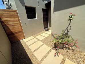 A courtyard with a wooden gate, a potted plant with pink flowers, and a tiled walkway. - Self-catering Pool-side Guesthouse (Cape Town)
