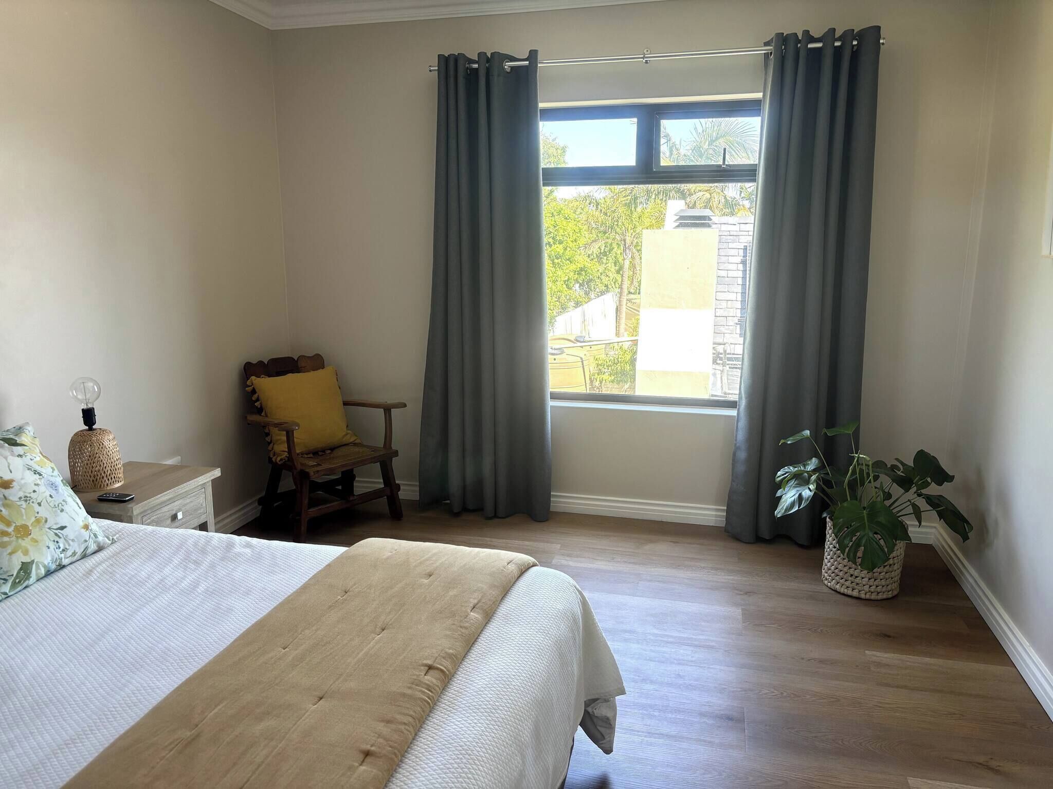 Une chambre à coucher avec un lit, une chaise, une table de chevet, une lampe et une fenêtre avec des rideaux.