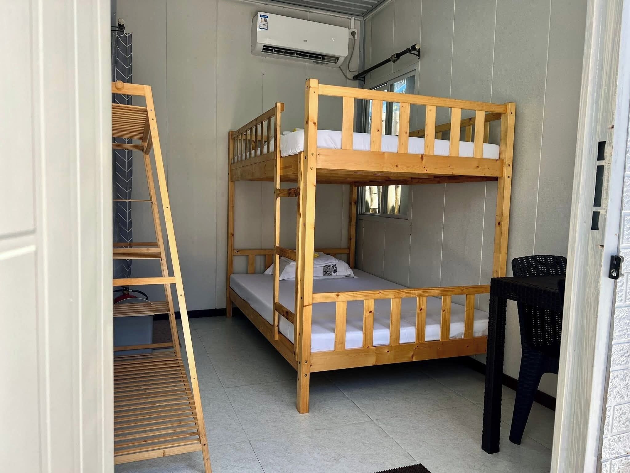 Dormitorio con literas, una escalera, una silla y un equipo de aire acondicionado.