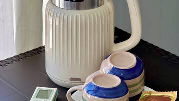 A white electric kettle, two striped cups, a small digital device, and a packet of tea on a table.