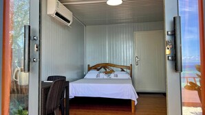 Una habitación con cama, una silla, aire acondicionado, una puerta y vista a la playa.