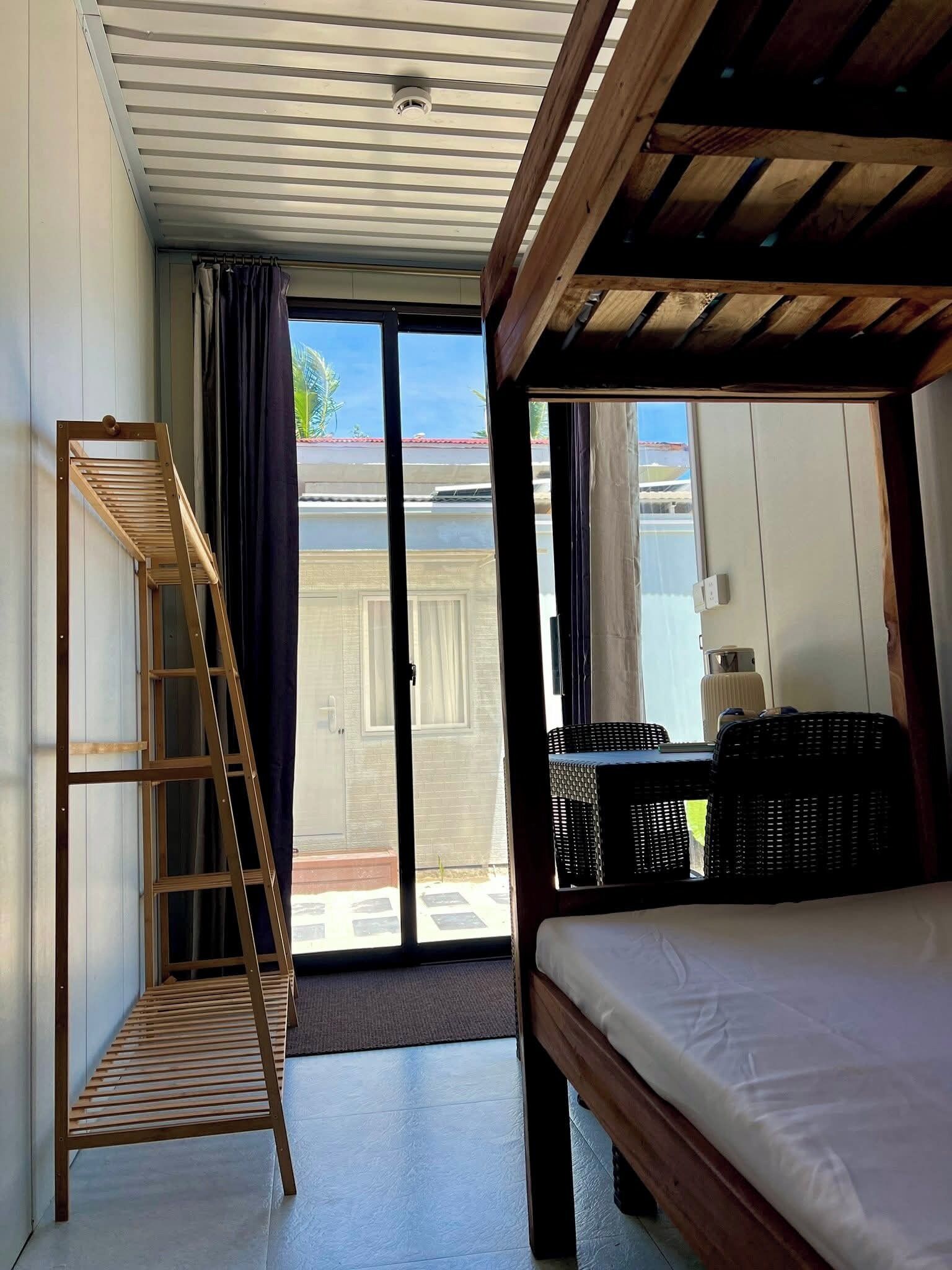 A room with a bed, a wooden ladder, a sliding glass door, and wicker furniture.