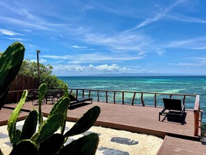 A wooden deck with chairs overlooking a turquoise sea, a wooden fence, and a cactus plant in the foreground. - Crossa Inn Siquijor (Siquijor)