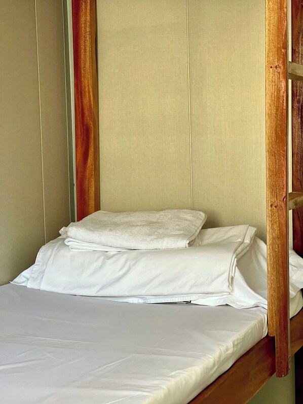 A single bed with white linens, a wooden headboard, and a plain wall.