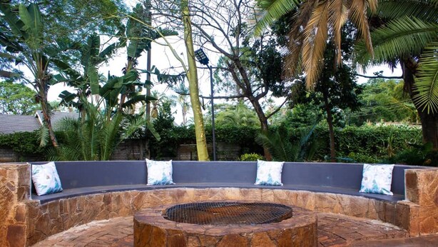A stone bench with cushions, a circular fire pit, and surrounding greenery.