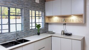 A kitchen with a stone backsplash, a sink, cabinets, and a countertop with a plant and kitchenware.