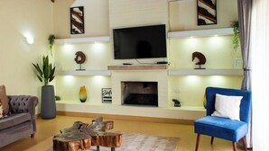 A living room with a fireplace, a television mounted above it, a blue armchair, and a grey sofa.