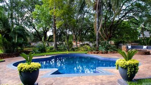 A swimming pool with a stone deck, surrounded by lush greenery and trees.