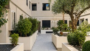 Un patio central con un camino principal, flanqueado por macetas y árboles, rodeado de edificios con múltiples ventanas.