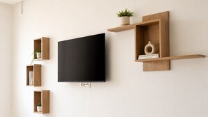Una sala de estar moderna con un televisor de pantalla plana montado en la pared, rodeada de estanterías de madera con objetos decorativos y plantas.