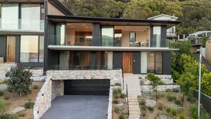 Ein modernes, zweistöckiges Haus mit Natursteinfassade, großen Fenstern und einer Auffahrt, die zu einer Garage führt.