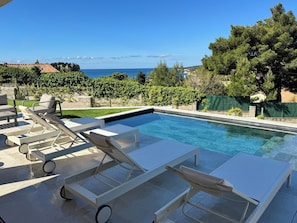 Piscina com espreguiçadeiras, vista para o mar e uma parede de pedra.