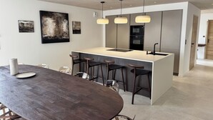 Una cucina moderna con isola centrale, sgabelli da bar, lampade a sospensione e un tavolo da pranzo con sedie.
