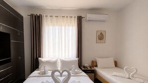 Une chambre d’hôtel avec un grand lit, un plus petit lit, une armoire, un appareil de climatisation et une fenêtre avec des rideaux.