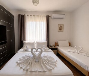 Ein Hotelzimmer mit einem großen Bett, einem kleineren Bett, einem Kleiderschrank, einer Klimaanlage und einem fenster mit Vorhängen.