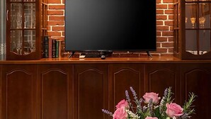 Un mur en briques sur lequel est fixé un téléviseur à écran plat, au-dessus d’un meuble en bois doté de portes en verre.