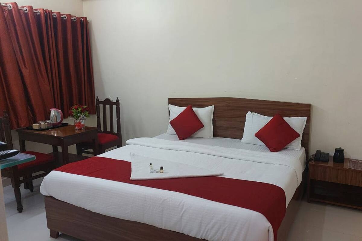 A hotel room with a large bed, two pillows, a bedside table, a chair, a desk, and a telephone.