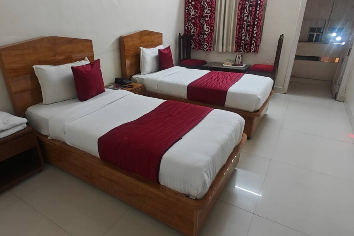A hotel room with two beds, wooden headboards, white bedding, red accents, a small bedside table, and a nightstand.