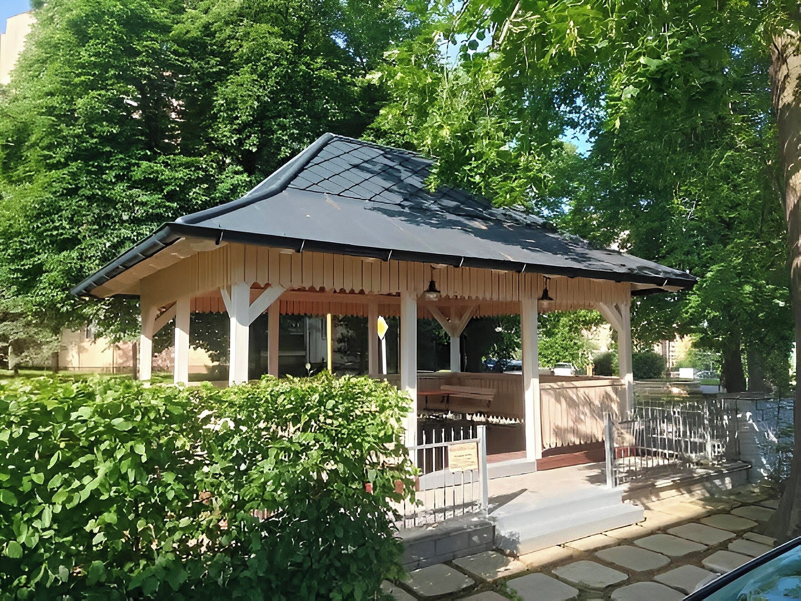 A gazebo with a tiled roof, surrounded by greenery and a stone pathway.