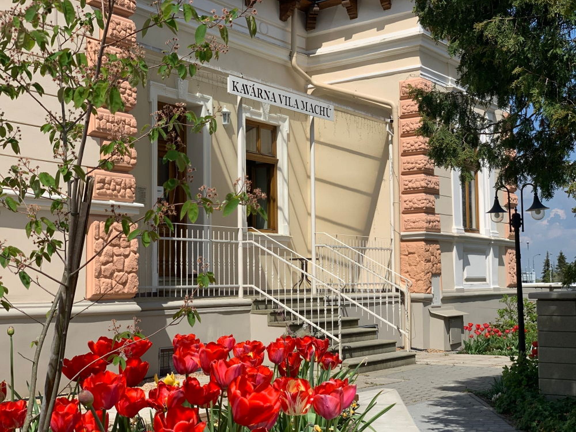 A building with a sign reading 'KAVÁRNIA VILÁM MACHÚ' and a white staircase leading to the entrance.