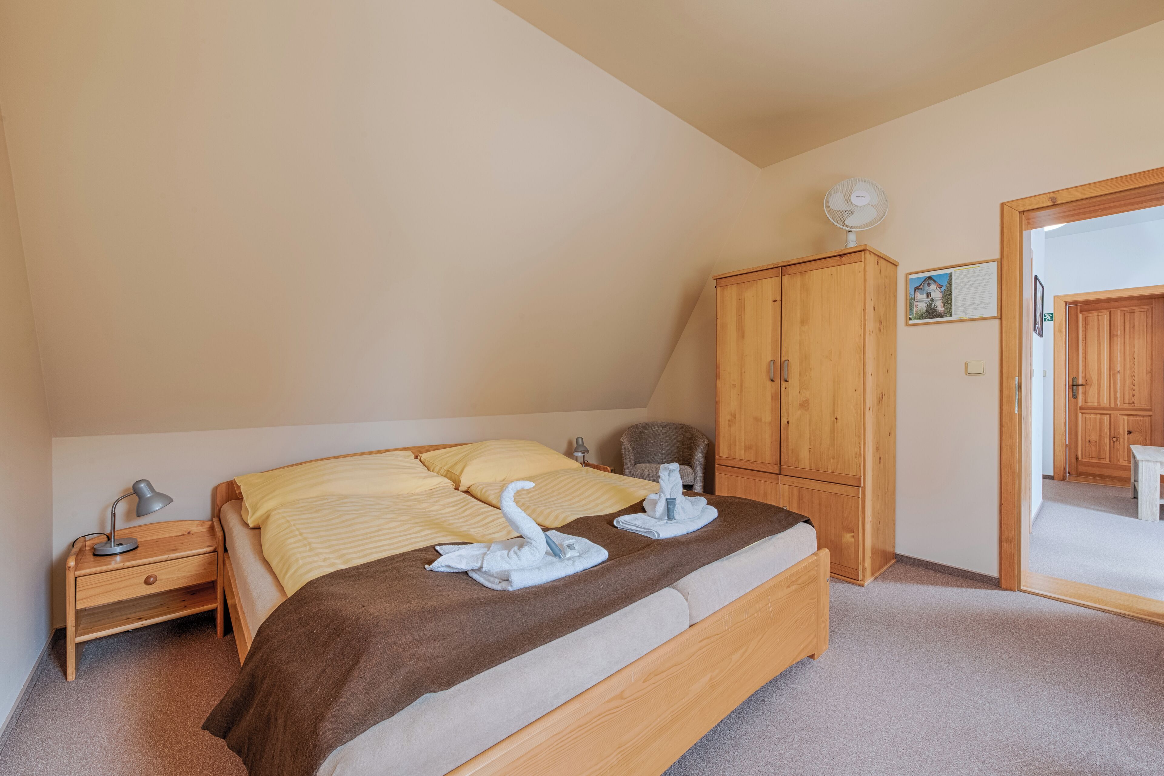A bedroom with a bed, wooden wardrobe, bedside table, and a fan.