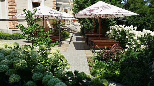 A courtyard with outdoor seating, umbrellas, and a building with a stone facade. - Penzion Vila Machů (Kopřivnice)