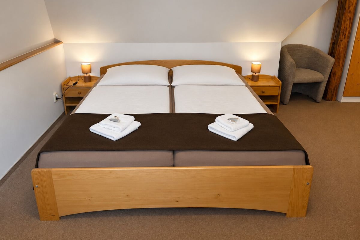 A double bed with a brown headboard and footboard, two bedside tables with lamps, a chair, and a wooden wall panel.