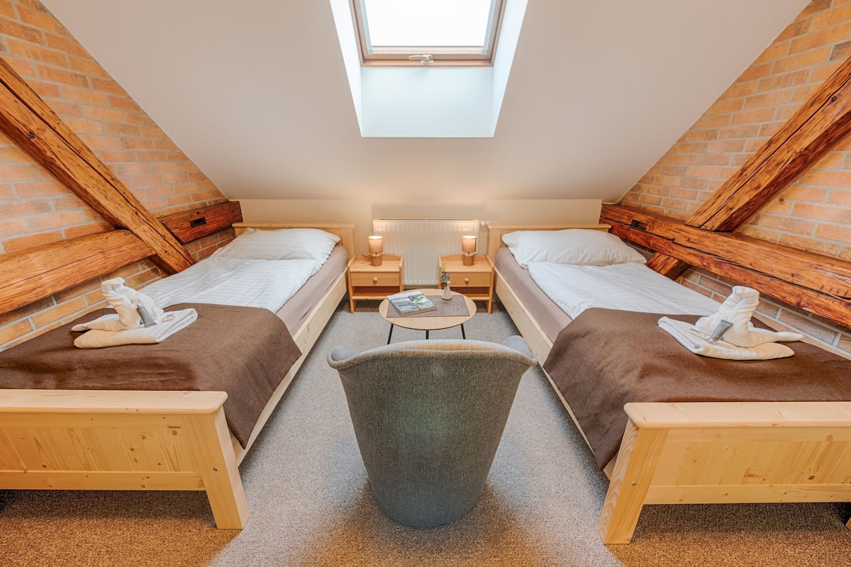 A room with two beds, a small table, a bench, and a skylight.