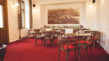 Una stanza con tavoli e sedie rotondi, un tappeto rosso, una grande fotografia aerea incorniciata e una libreria con libri.