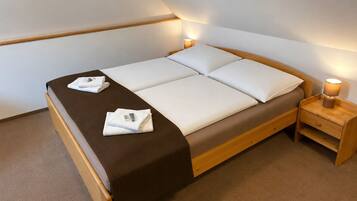 A single bed with a brown headboard, white bedding, and two towels on the bed. There is a wooden nightstand with a lamp beside the bed.