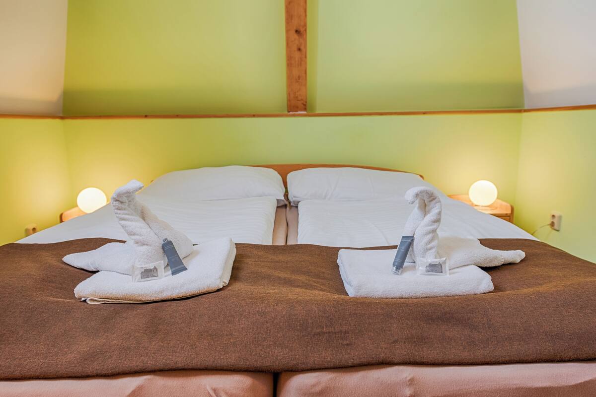 A double bed with two towels and a bottle on each side, a wooden headboard, and a green wall.
