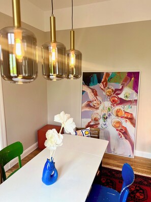 A dining area with a white table, blue vase, green and red chairs, and a painting on the wall. - Luxury old building within walking distance of the city center - Lübeck's best location - water view (Lübeck)