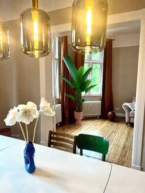 A dining area with a table, chairs, a vase with flowers, a potted plant, and hanging light fixtures. - Luxury old building within walking distance of the city center - Lübeck's best location - water view (Lübeck)